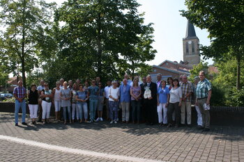 Das Bild zeigt die Ratsleute aus der Partnergemeinde Losser zu Besuch in Emsbüren im Jahr 2015 in einem Gruppenfoto vor dem Kirchturm Emsbüren mit Bürgermeister Bernhard Overberg